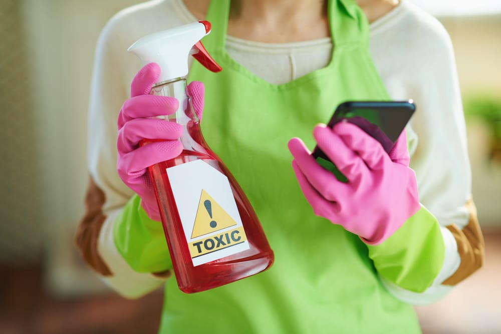 Woman holding a toxic cleaning product while searching safe alternatives like Clean Habits