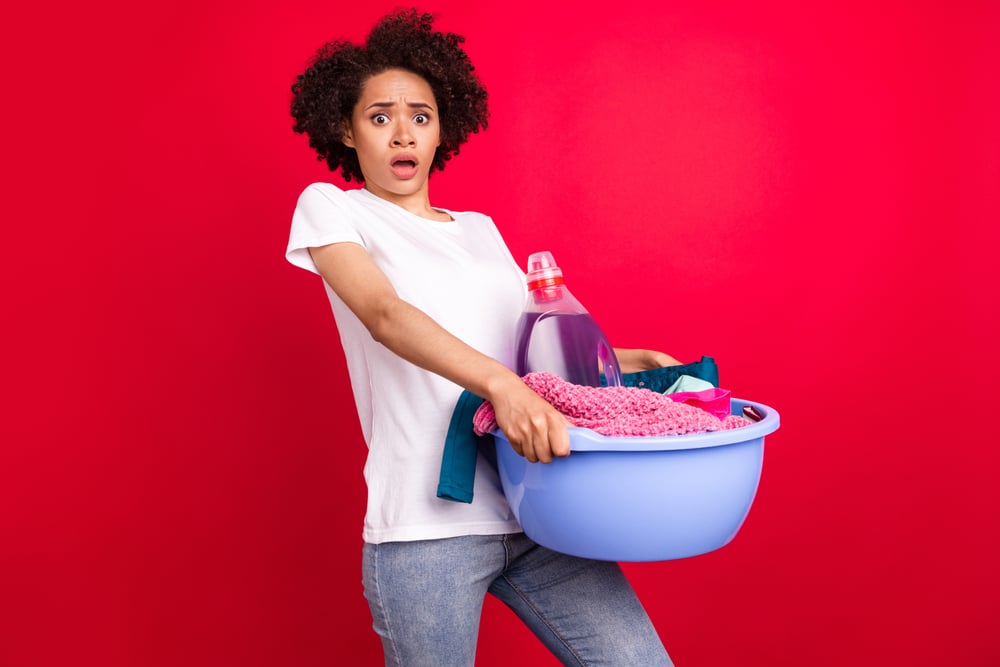 Woman holding laundry detergent with skin-irritating ingredients and making a stressed expression