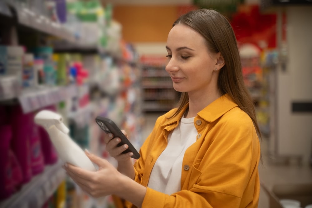Woman holding a disinfectant cleaning product and searching for non-toxic alternatives on her phone